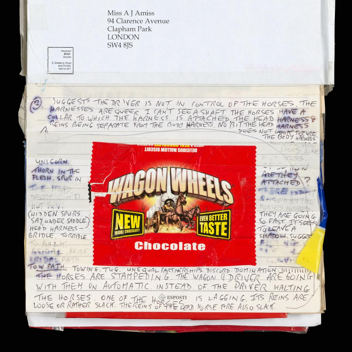 Photograph of an open page of a lined scrapbook set against a black background. In the centre of the page a chocolate biscuit wrapper has been stuck down. It is branded 'Wagon Wheels', is bright red in colour and caries an illustration in the centre of a Wild West wagon speeding through the desert, horses mid-gallop. Surrounding the wrapper are copious handwritten notes in block caps. The text analyses in great detail the illustration on the wrapper, making descriptions, observations and conclusions. Some of the ink has bled into the page and some is obscured by sticky tape.