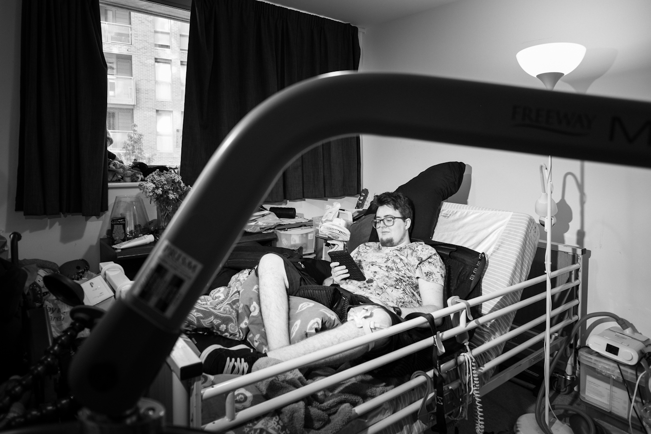 Black and white photograph of an individual at home lying in bed reading.