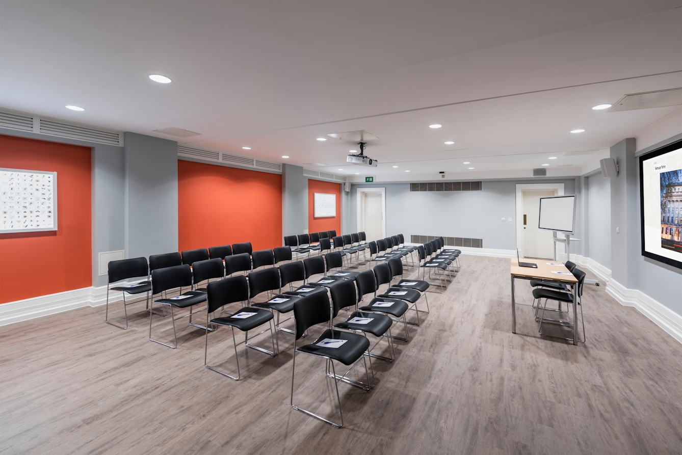 Photograph of the Burroughs room at the Wellcome Collection.
Photograph shows a theatre set-up, with a presenting screen and whiteboard at the front of the room.