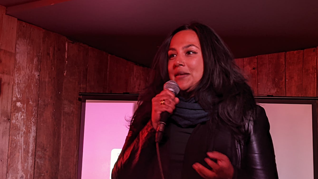 .Subhadra Das speaking into a handheld microphone in front of a screen.