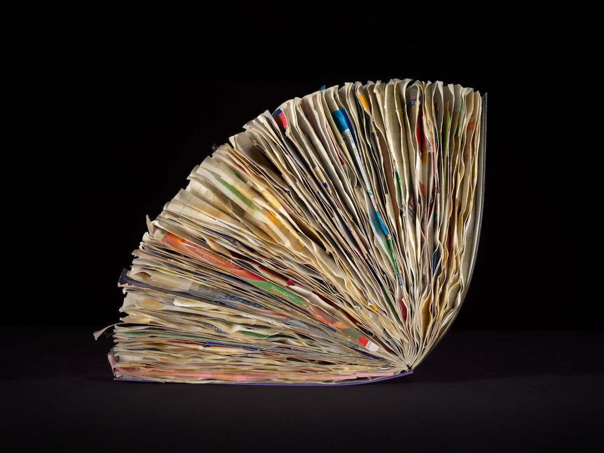 Side view of a large ring-bound scrapbook on a black background. The scrapbook is bulging with ephemera pasted within it.