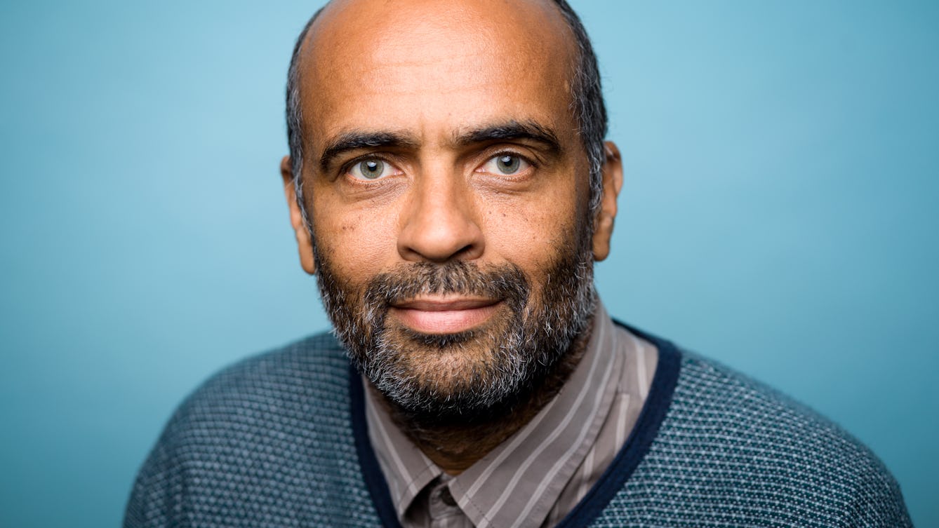 Photographic portrait showing the head and shoulders of Martin Glover against a blue background.