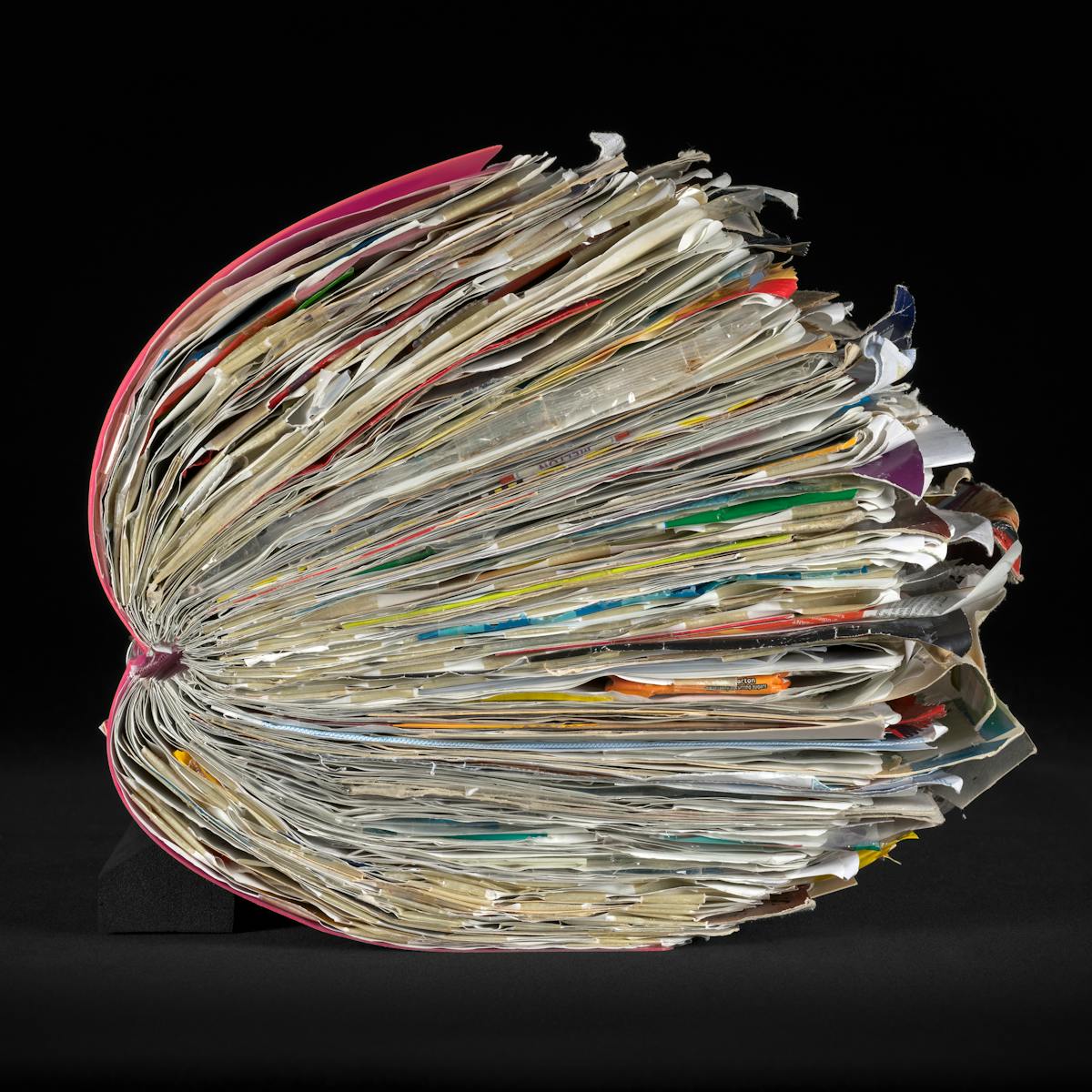 Side view of a large ring-bound scrapbook on a black background.  The scrapbook is bulging with ephemera pasted within it.  