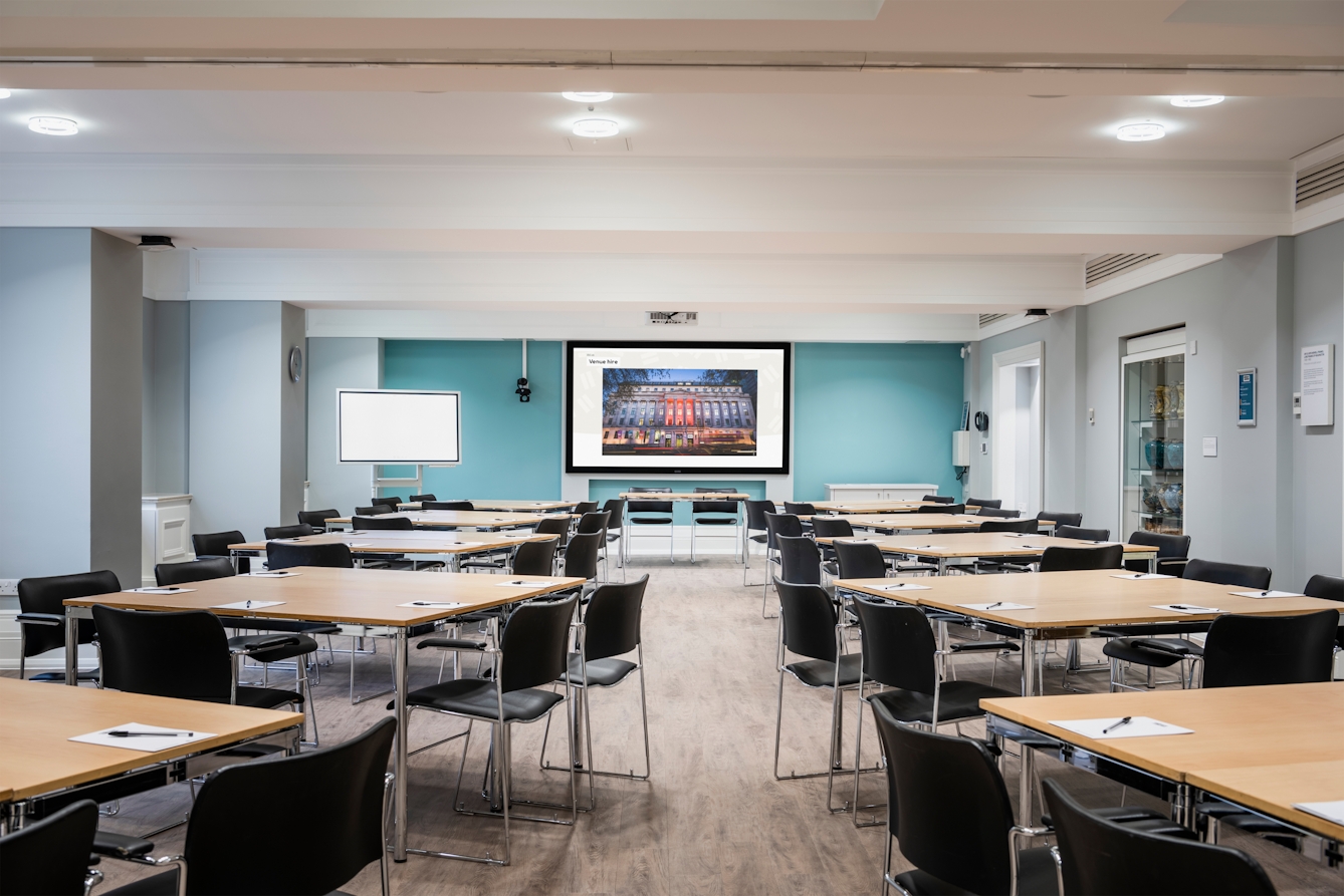 Photograph of the Franks and Steel room at the Wellcome Collection.
Photograph shows a cabaret set-up, with desks placed in small groups and a whiteboard and presenting screen at the front of the room.
