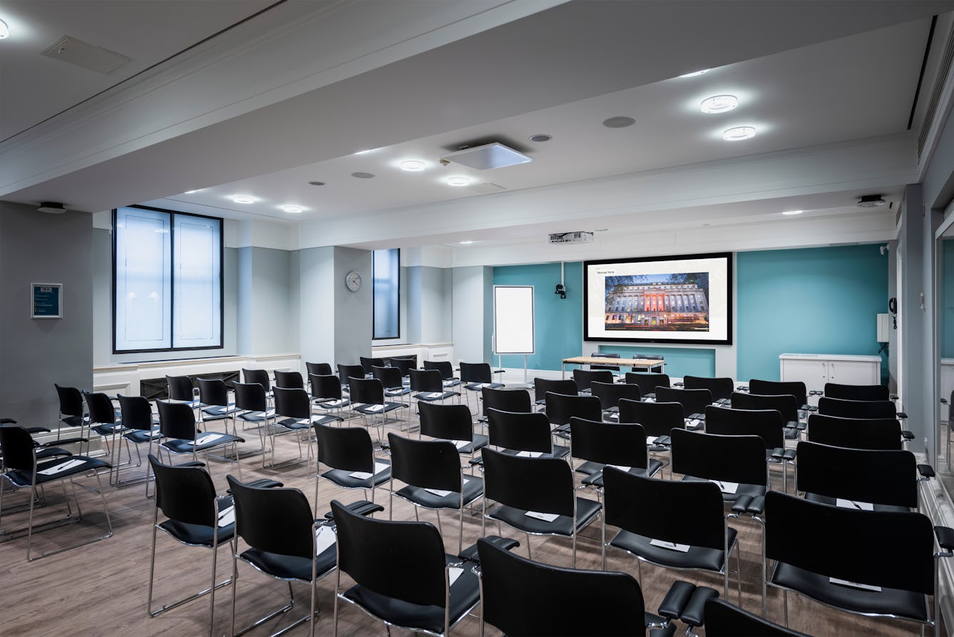 Photograph of the Franks and Steel room at the Wellcome Collection.
Photograph shows a theatre space with chairs and a projector and screen set-up. There are large windows in the room.