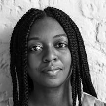 Balck and white photograph of the head and shoulders a young black woman with long braided hair. She is looking directly at the camera.