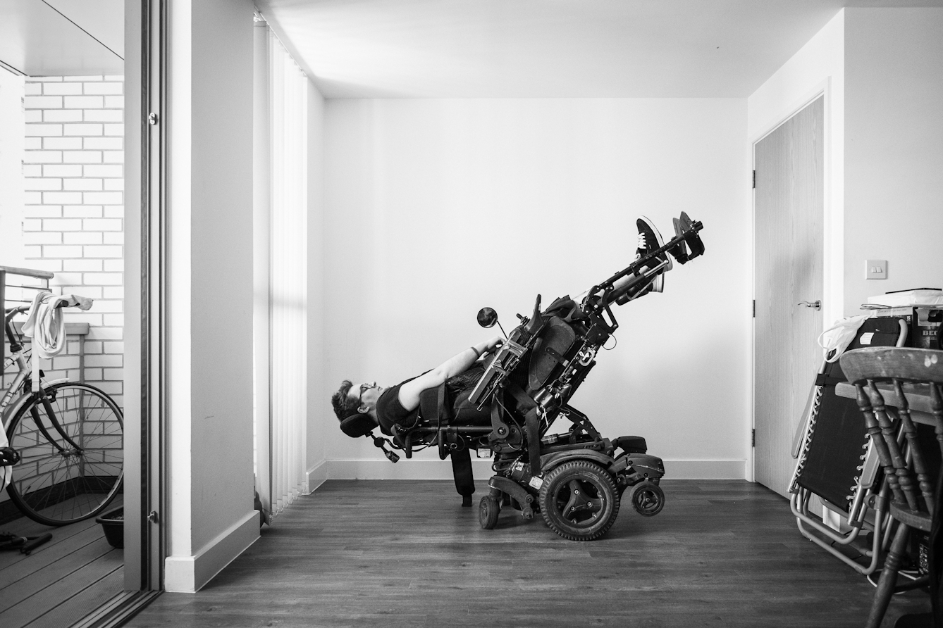 Black and white photograph of an individual in an electric wheelchair, reclining it right the way back.