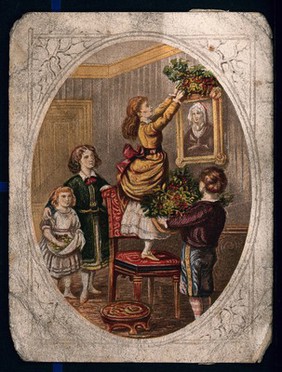 A child holds a large bunch of holly and two others watch as a young woman stands on a chair to reach the picture she is decorating for Christmas. Colour process print.