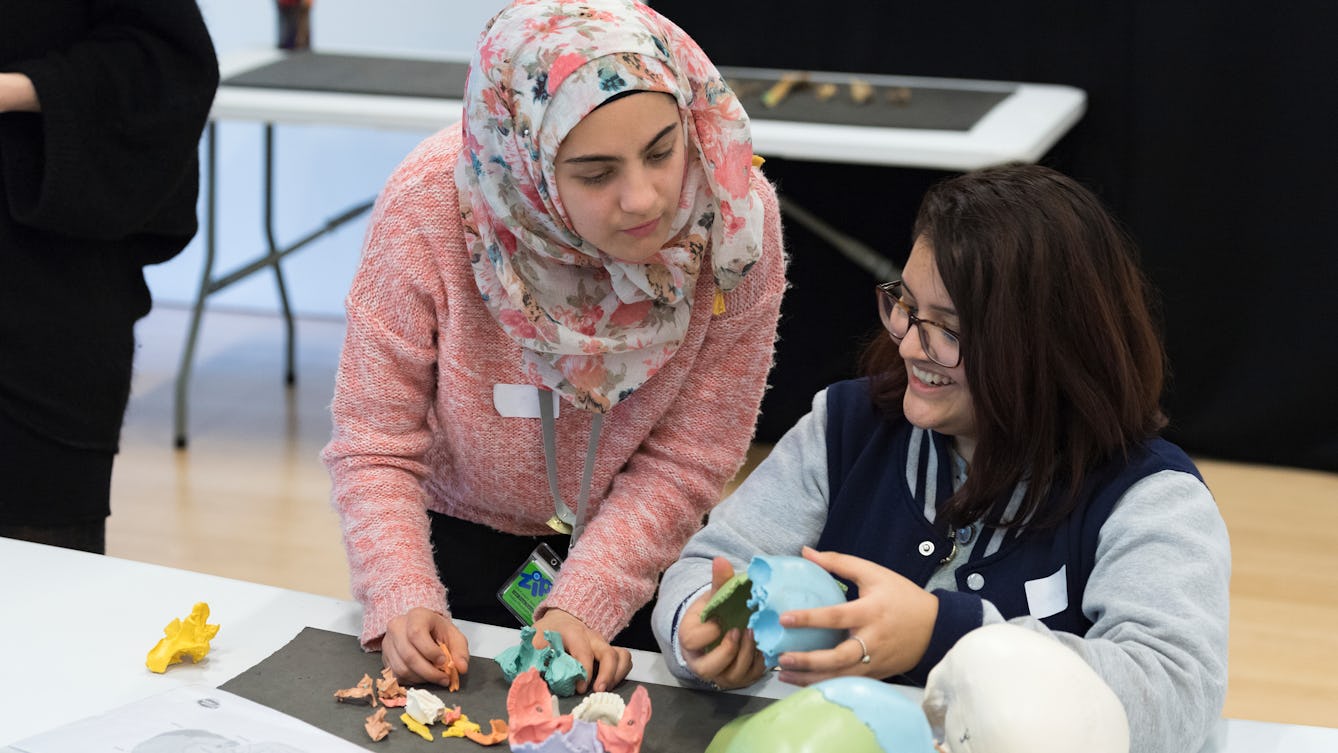 Two young people at a table working holding part of a colourful plastic skull.