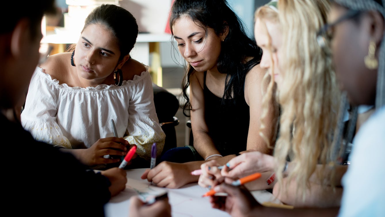 Young people sitting around a table with pens and paper.