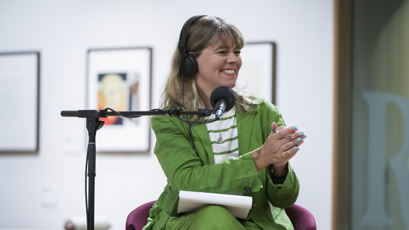 Claudia Hammond sitting in front of a standing microphone and wearing headphones smiling and clapping.